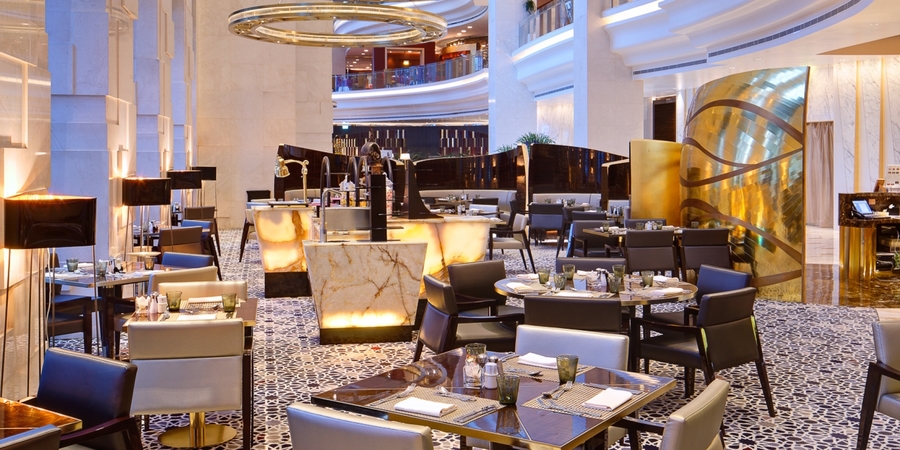 An open dining room with marble center tables, gold details, bespoke wood dining tables and white and black leather armchairs. hba HBA &#8211; The Best Interior Design Projects in Dubai HBA2